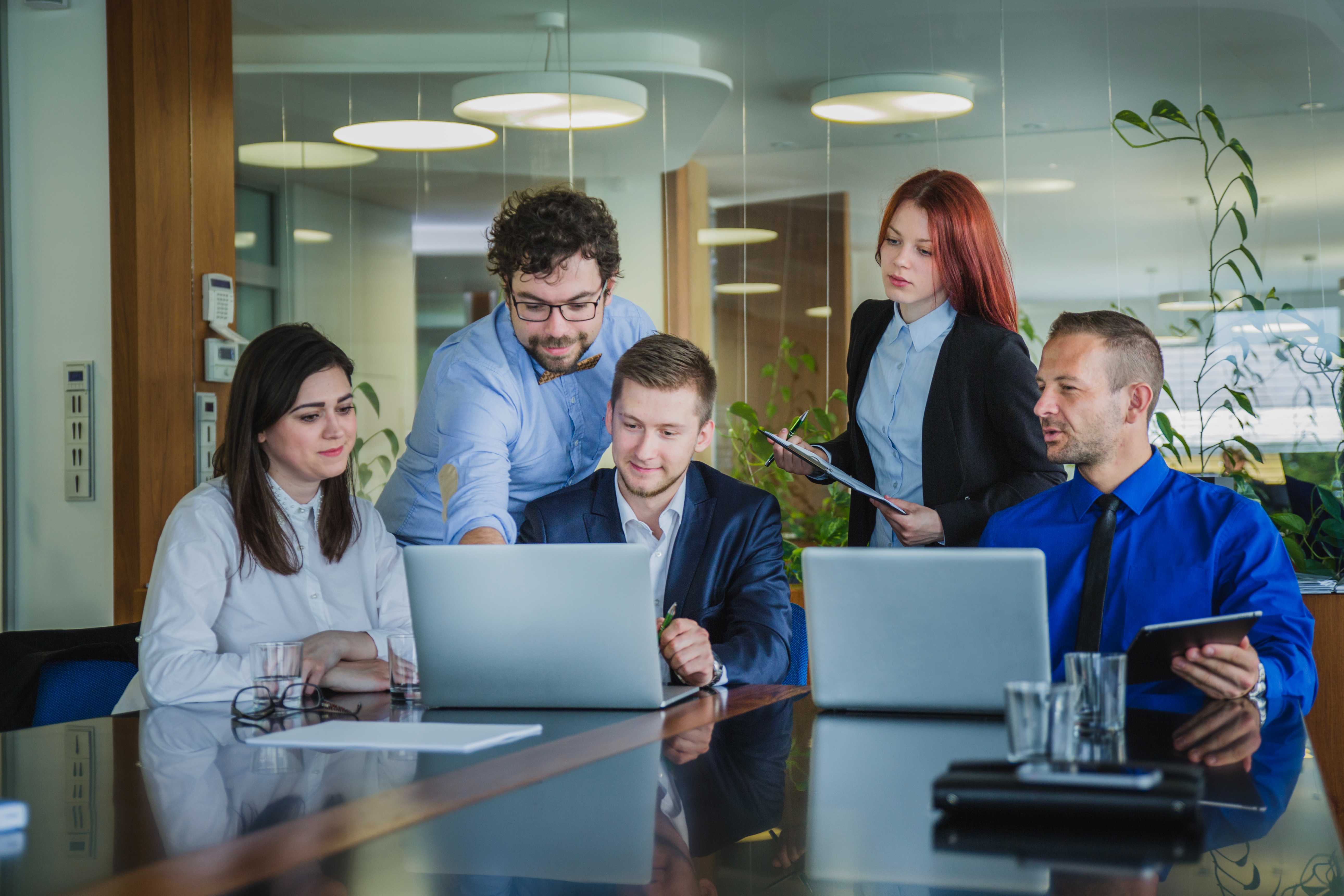 A group of professionals in a meeting room discussing charts and graphs displayed on tablets and papers.